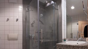 Un baño moderno con ducha acristalada, inodoro blanco y lavamanos de granito.