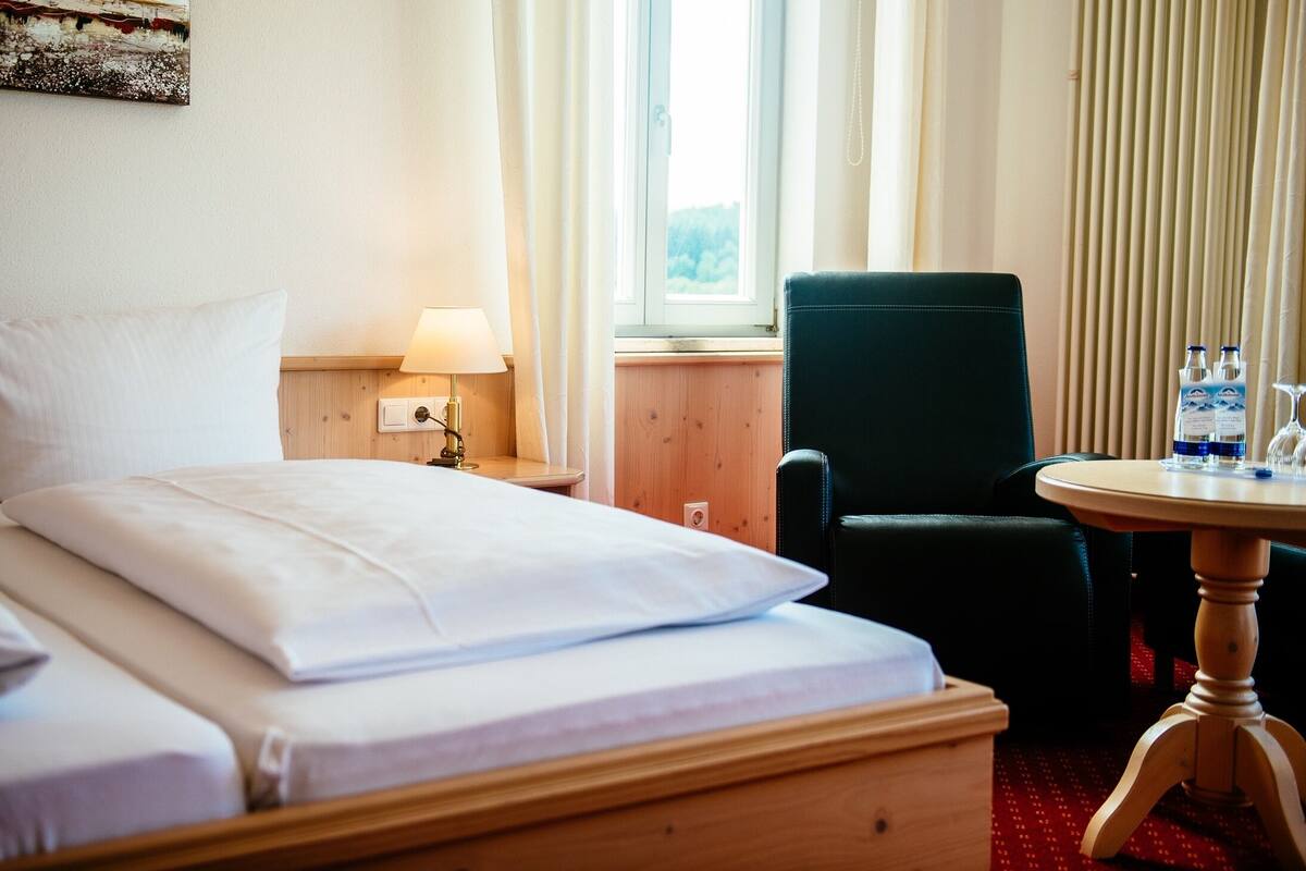 A hotel room with a bed, a chair, a table, a lamp, and a window with curtains.