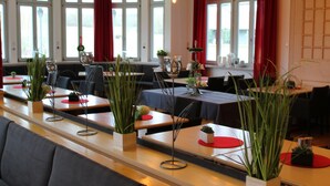 Un restaurante con mesas largas, detalles en rojo y plantas en macetas.