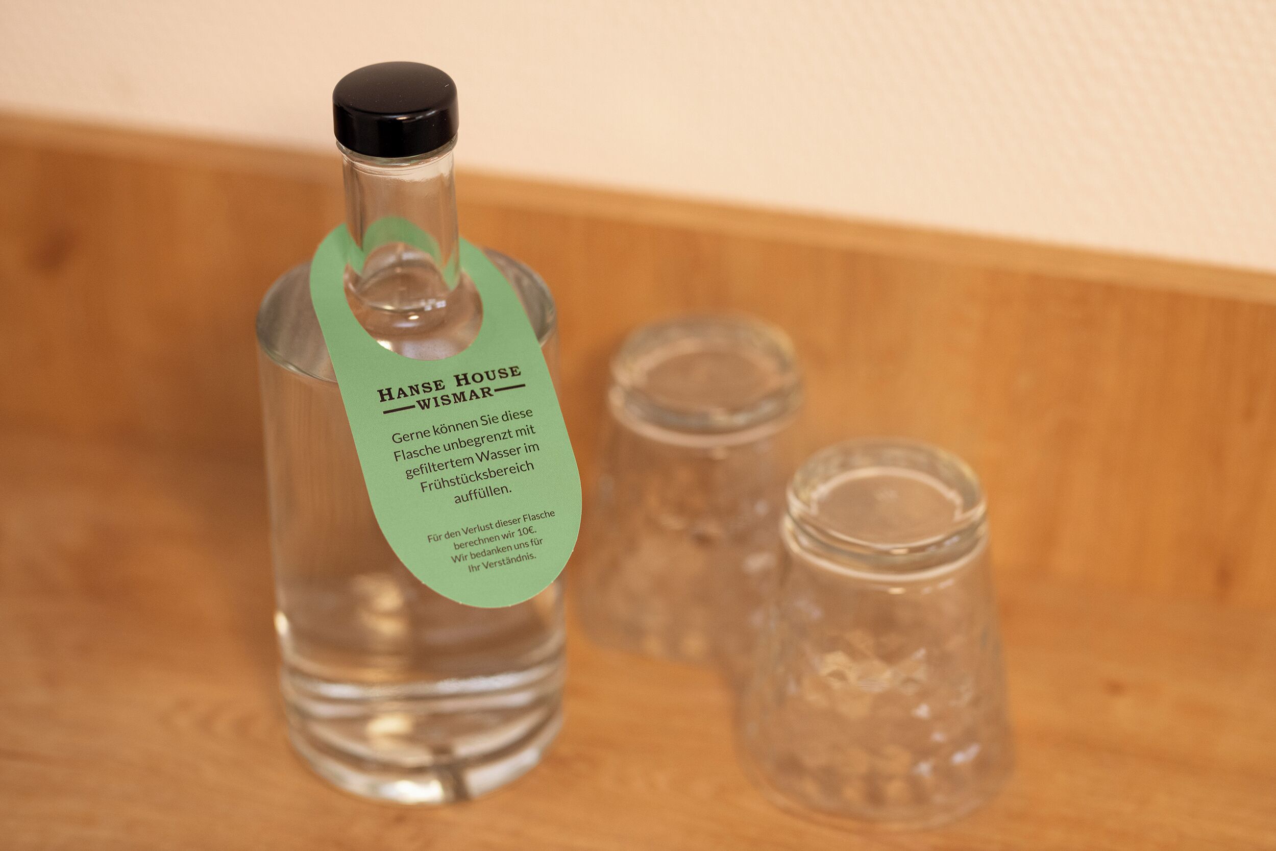 Una bottiglia d'acqua Hans Haus Wismar con etichetta verde, posizionata su una superficie in legno accanto a due piccoli vasetti di vetro.