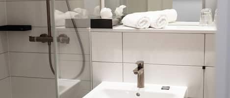 A bathroom with a shower, a sink, and a mirror. There are towels and toiletries on the sink.