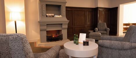A cozy living room with patterned armchairs, a fireplace, and a round table with bottles and a menu.