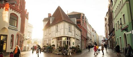 Eine Kopfsteinpflasterstraße, gesäumt von historischen Gebäuden, darunter ein Fachwerkhäuschen und ein Geschäft mit dem Schild 'Ratsapotheke'.