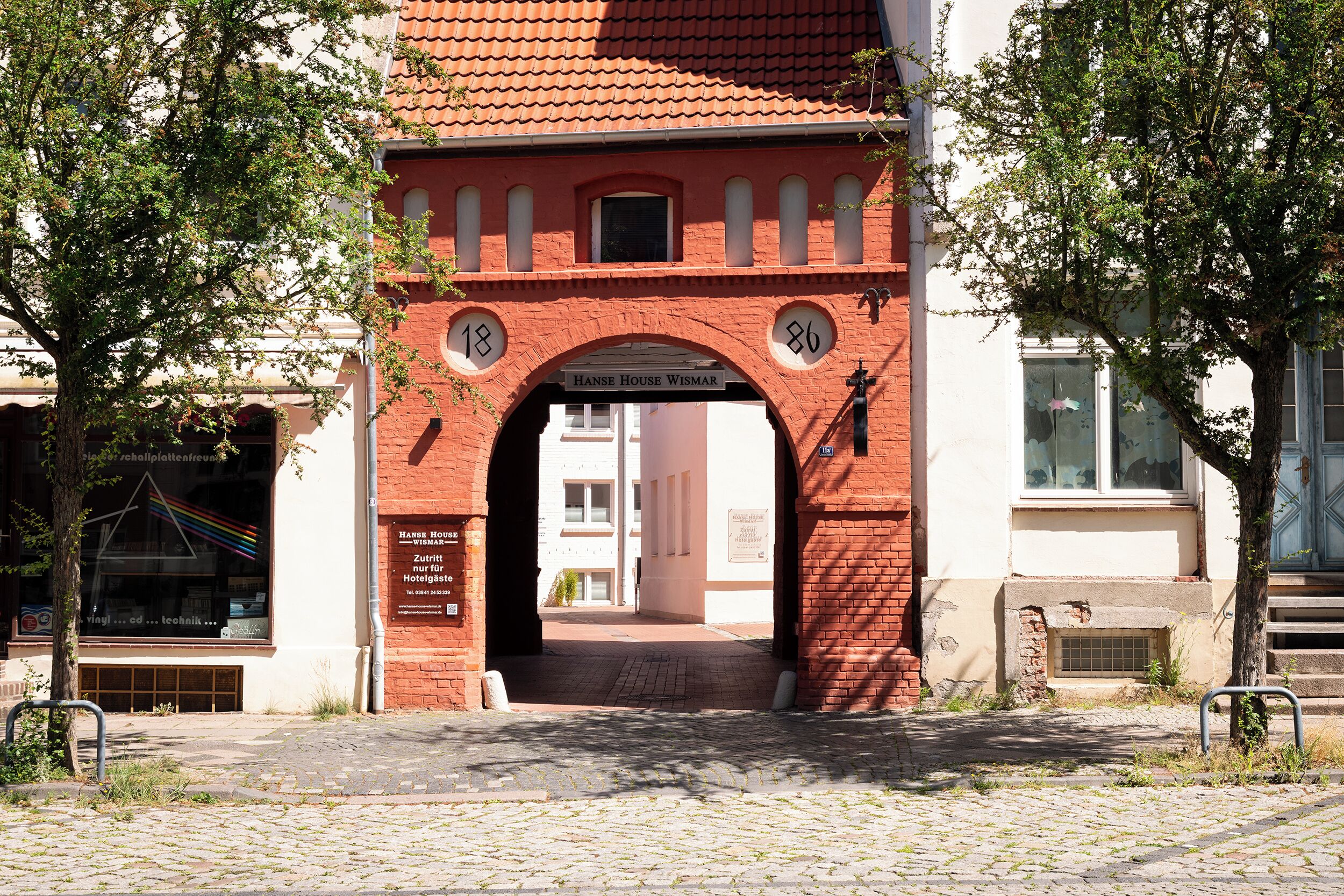 A brick archway with the numbers 18 and 86, leading to a building with a sign that reads 'HANSE HOUSE WISMAR'.