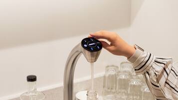 A hand adjusting a faucet with a digital interface, a glass carafe, and a row of glasses on a shelf.