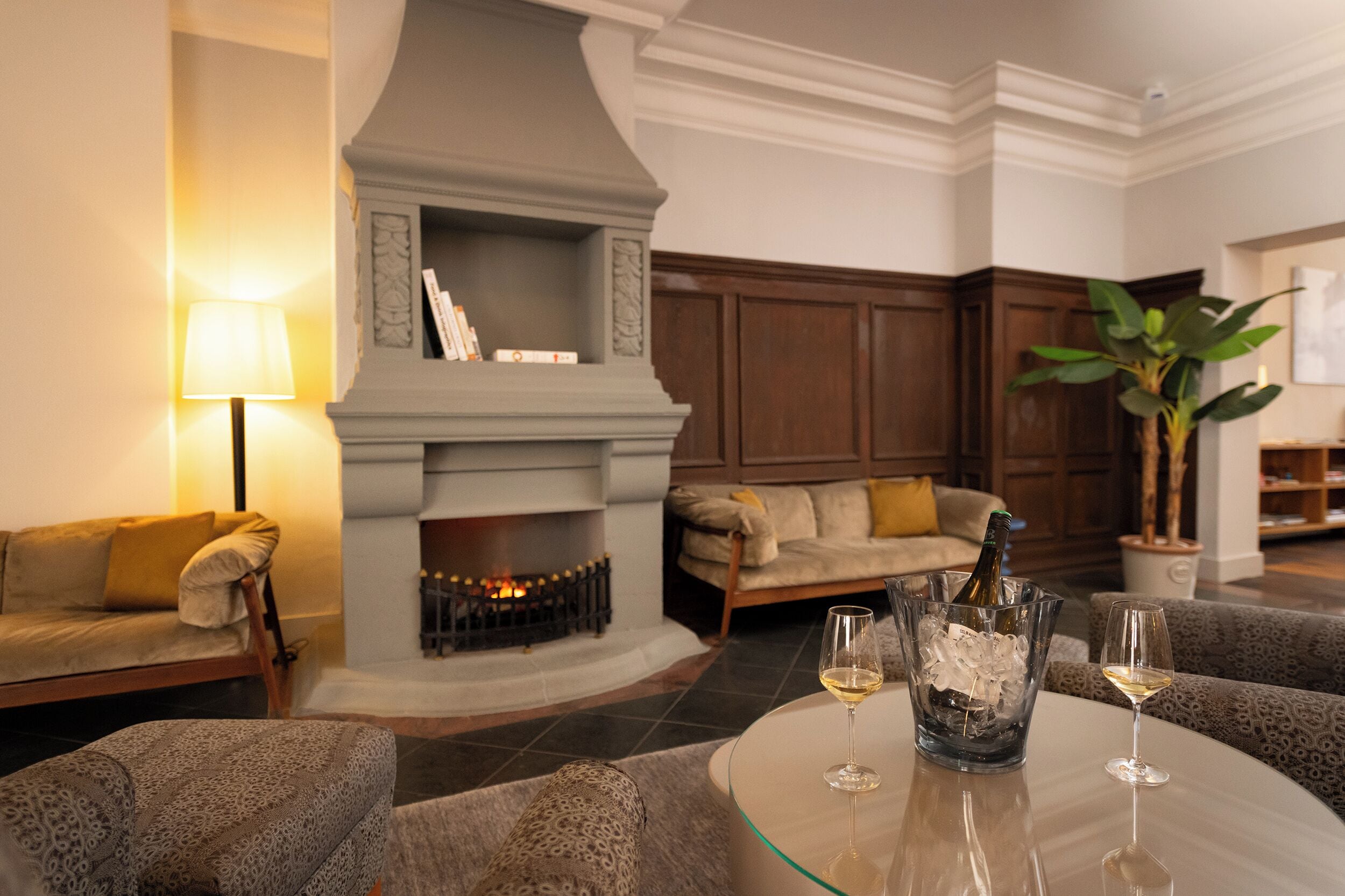 A modern living room with a fireplace, sofas, a coffee table with wine glasses, and a potted plant.