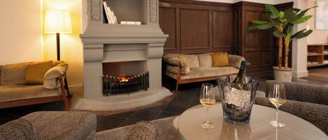 A modern living room with a fireplace, sofas, a coffee table with wine glasses, and a potted plant.