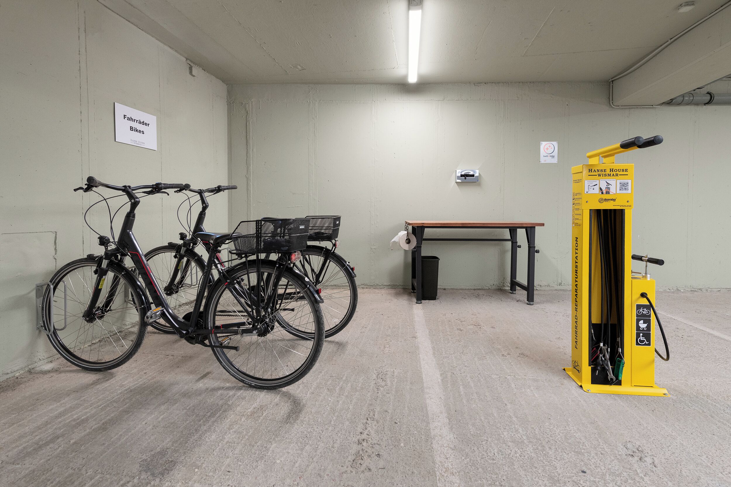 A bicycle parking area with two bicycles, a table, and a yellow bicycle repair station.