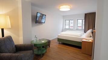 Een hotelkamer met een bed, een tv die aan de muur is bevestigd, een groen bijzettafeltje, een lamp en een raam met gordijnen.