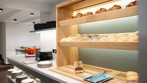 Un comptoir pour le petit-déjeuner avec des croissants, des viennoiseries et du pain. On y trouve des assiettes et une machine à café.