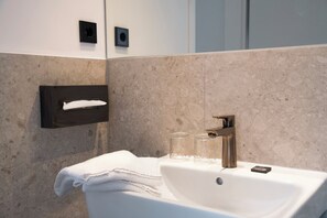 Un baño moderno con un lavabo blanco, un perchero y dos vasos de vidrio transparente sobre el lavabo.