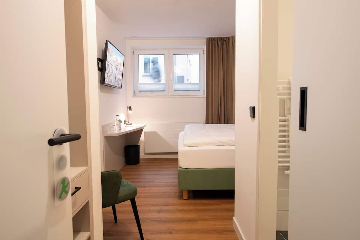 A compact hotel room with a bed, a desk, a chair, and a window with curtains.