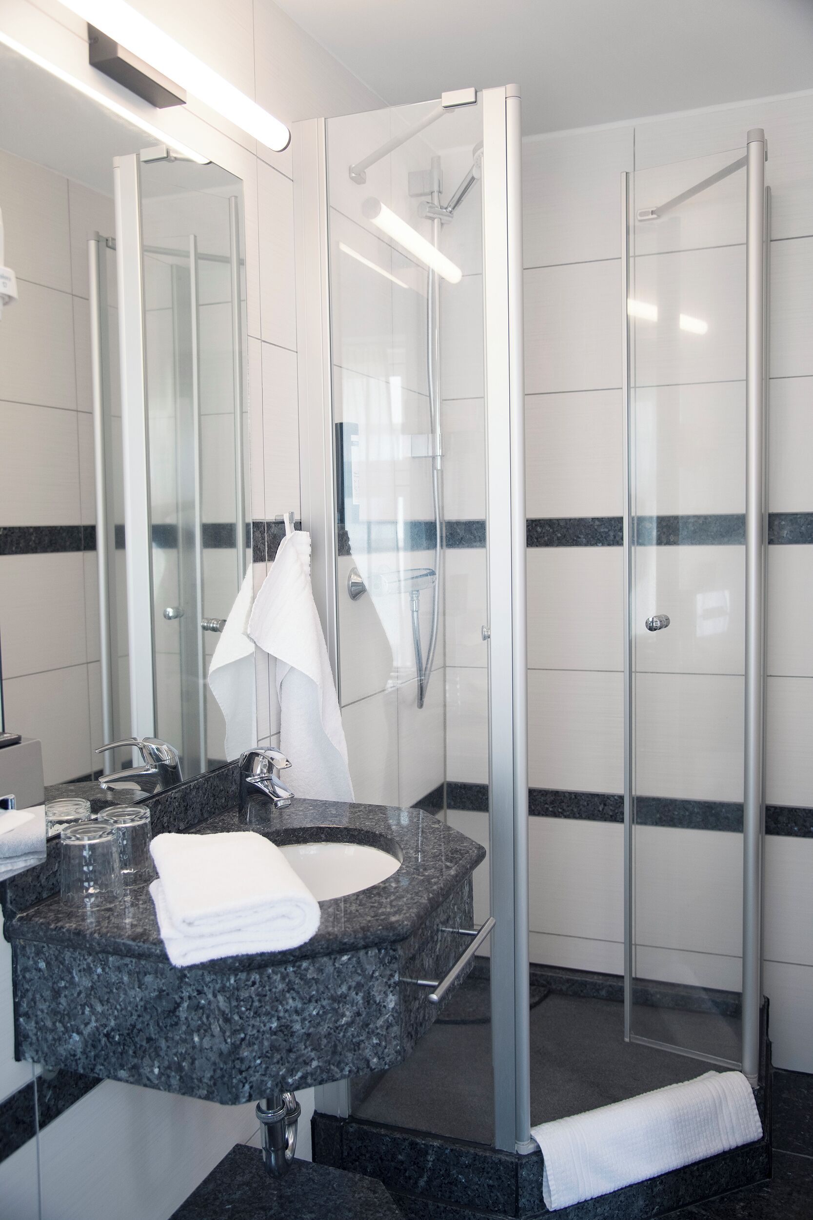 A modern bathroom with a granite countertop, a glass shower enclosure, and a large mirror.