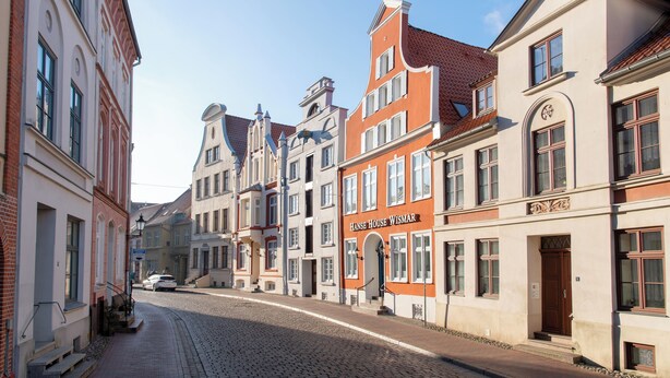 Une rue pavée bordée de bâtiments historiques, dont l’un porte l’inscription « Hans House Wismar ».