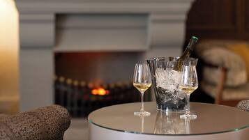 Une cheminée avec un feu de bois, une table avec une bouteille de champagne et deux verres, et des fauteuils à motifs.