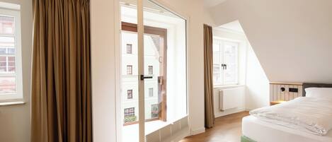 A bedroom with a large window, a bed, and a sliding door leading to an outdoor balcony.