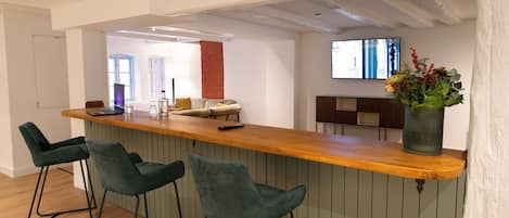 A modern kitchen with a wooden bar, green bar stools, and a large vase of flowers.