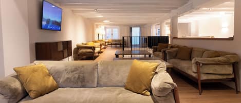A spacious living area with two sofas, a coffee table, and a flat-screen TV mounted on the wall.
