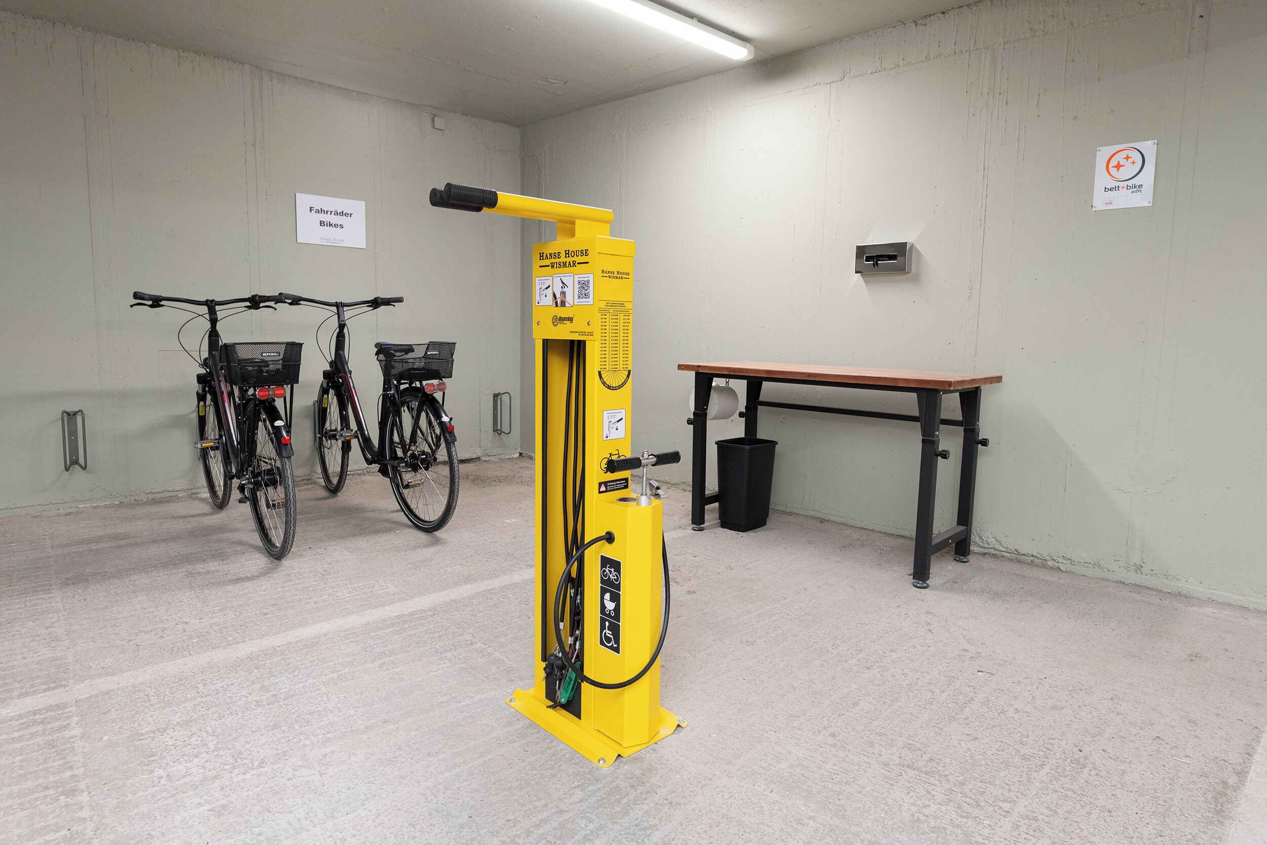 A bike rental station with two bicycles, a yellow bike pump, and a bench.