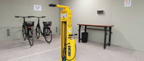Uma estação de aluguel de bicicletas com duas bicicletas, uma bomba de bicicleta amarela e um banco.