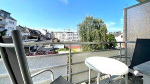 A balcony with a table and chairs, overlooking a street with buildings and a tree.