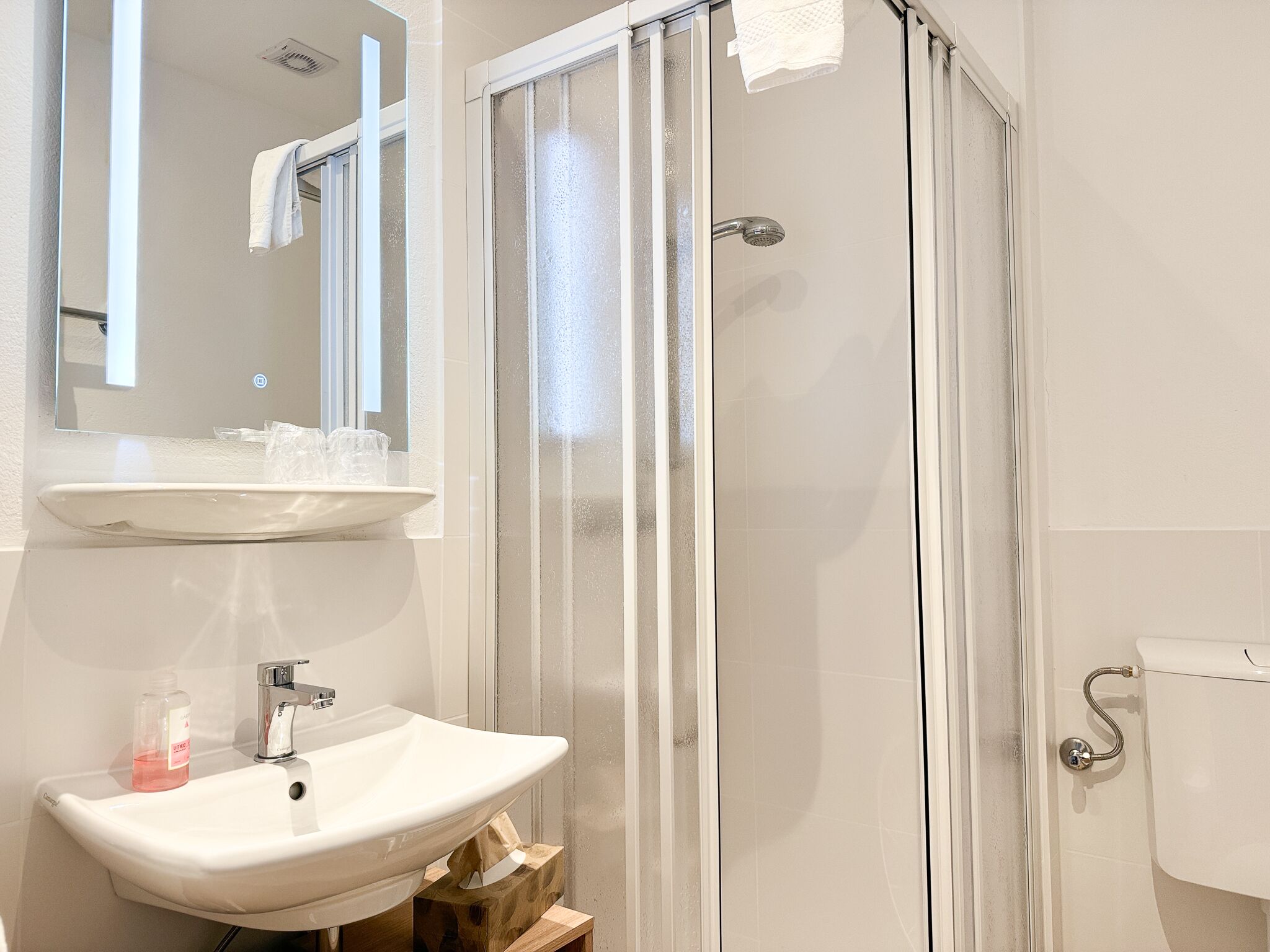 A bathroom with a white sink, a mirror, a glass shower enclosure, and a toilet.