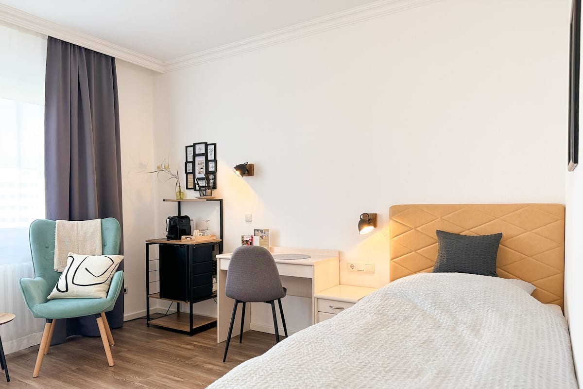 A hotel room with a bed, a desk, a chair, and a small table.