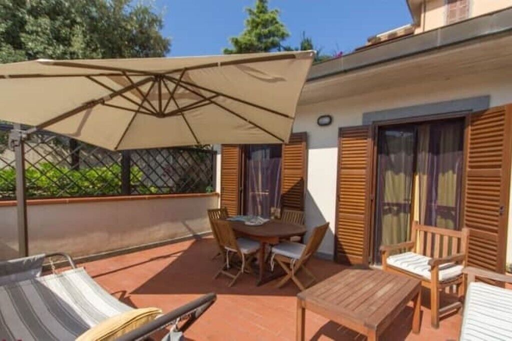 Une terrasse avec une table et des chaises, une table en bois et un fauteuil de jardin à rayures.