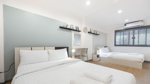 Ein modernes Hotelzimmer mit einem großen Bett, einem Einzelbett, einem Schreibtisch mit Stuhl, einem Nachttisch mit Lampe und einem Fenster mit Jalousien.