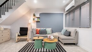 Ein modernes Wohnzimmer mit Treppe, einem grauen Sofa, einem Schaukelstuhl und einem Couchtisch.