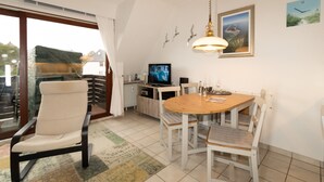 Un comedor con una mesa redonda, sillas, televisor y una ventana con cortinas.