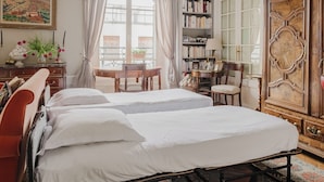 A bedroom with two beds, a wooden cabinet, a bookshelf, and a dining area with a table and chairs.