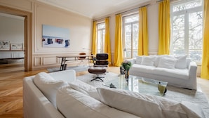 A modern living room with a white sofa, a glass coffee table, and yellow curtains. - Augustin Glory, by Veeve (Paris)