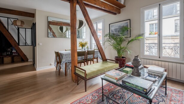 A spacious living room with a high ceiling, wooden beams, a dining area with a table and chairs, a large mirror, and a view of the outside balcony. - Wood Notes, by Veeve (Paris)