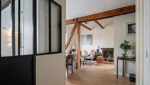 A spacious living area with wooden beams, a fireplace, and a dining area with a patterned tablecloth. - Wood Notes, by Veeve (Paris)