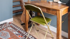 A room with a wooden desk, a green chair, a guitar, a framed picture, and a staircase. - Wood Notes, by Veeve (Paris)