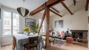 A dining area with a table set for four, wooden beams, a fireplace, and a view of the city through large windows. - Wood Notes, by Veeve (Paris)