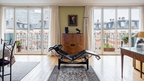 Una habitación amplia con un ventanal grande, un sillón reclinable, un armario de madera y un escritorio con lámpara.