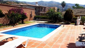 Una piscina con suelo de baldosas, rodeada de sillas de descanso y plantas en macetas.