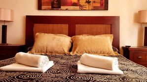 Habitación de hotel con una cama grande, dos almohadas, cabecero y una colcha estampada, además de un cuadro sobre la cama.