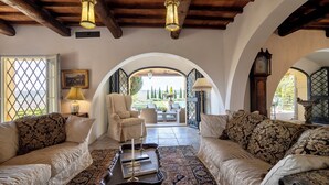 Ein gemütliches Wohnzimmer mit Kamin, zwei Sofas, einem Couchtisch und Blick auf den Garten durch einen Bogen.