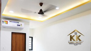 A bedroom with a bed, a ceiling fan, an air conditioning unit, and a logo on the wall. - K K Luxurious Home Stay (Garudeshwar)