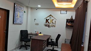 A reception area with a wooden desk, black office chairs, a brown sofa, and a ceiling with recessed lighting. - K K Luxurious Home Stay (Garudeshwar)