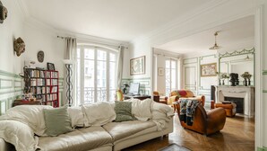 Un salon avec un canapé beige, un fauteuil en cuir, une bibliothèque et une cheminée.
