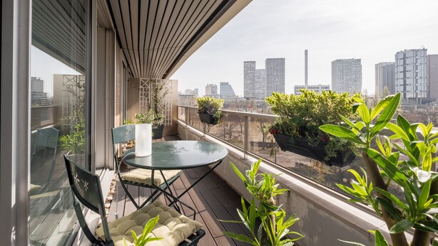 A balcony with a table and chairs, potted plants, and a city view. - Sights of the Seine, by Veeve (Paris)