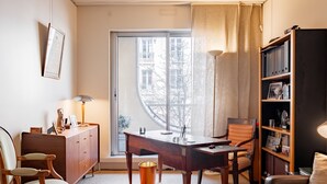 A cozy room with a wooden desk, a chair, a bookshelf, and a window with a view of buildings. - Sights of the Seine, by Veeve (Paris)