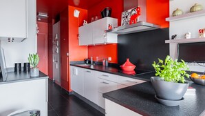 A modern kitchen with white cabinets, a black countertop, and red accents. - Sights of the Seine, by Veeve (Paris)
