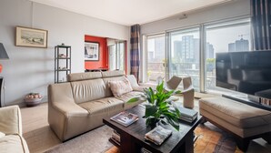 A modern living room with a beige sofa, a coffee table with magazines, a plant, and a TV. - Sights of the Seine, by Veeve (Paris)