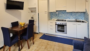A compact kitchen with white cabinets, a tiled backsplash, a built-in oven, and a dining area with a wooden table and chairs. - Beautiful two-bedroom apartment in a central location, just a few steps from the sea   (Giardini Naxos)