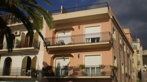 A multi-story building with balconies, air conditioning units, and a sign for a business named "Dharma." - Beautiful two-bedroom apartment in a central location, just a few steps from the sea   (Giardini Naxos)